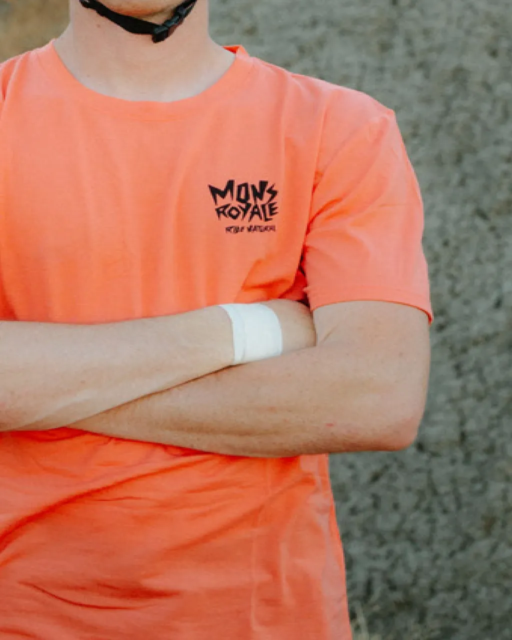 A person in a coral Mons Royale T-shirt stands with arms crossed and a white wristband.
