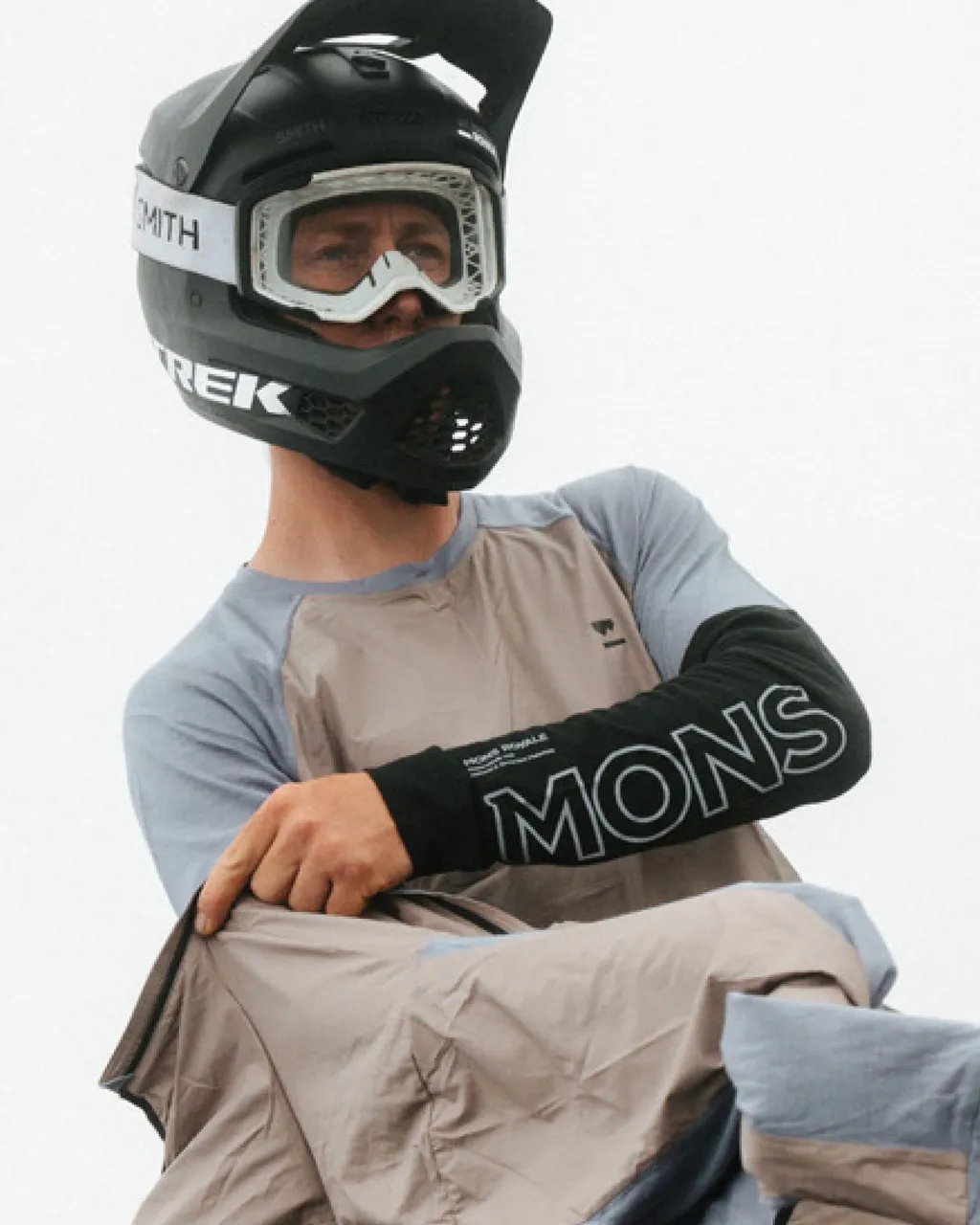 A helmeted mountain biker sits in a grey and blue Mons Royale jersey with logo sleeves.
