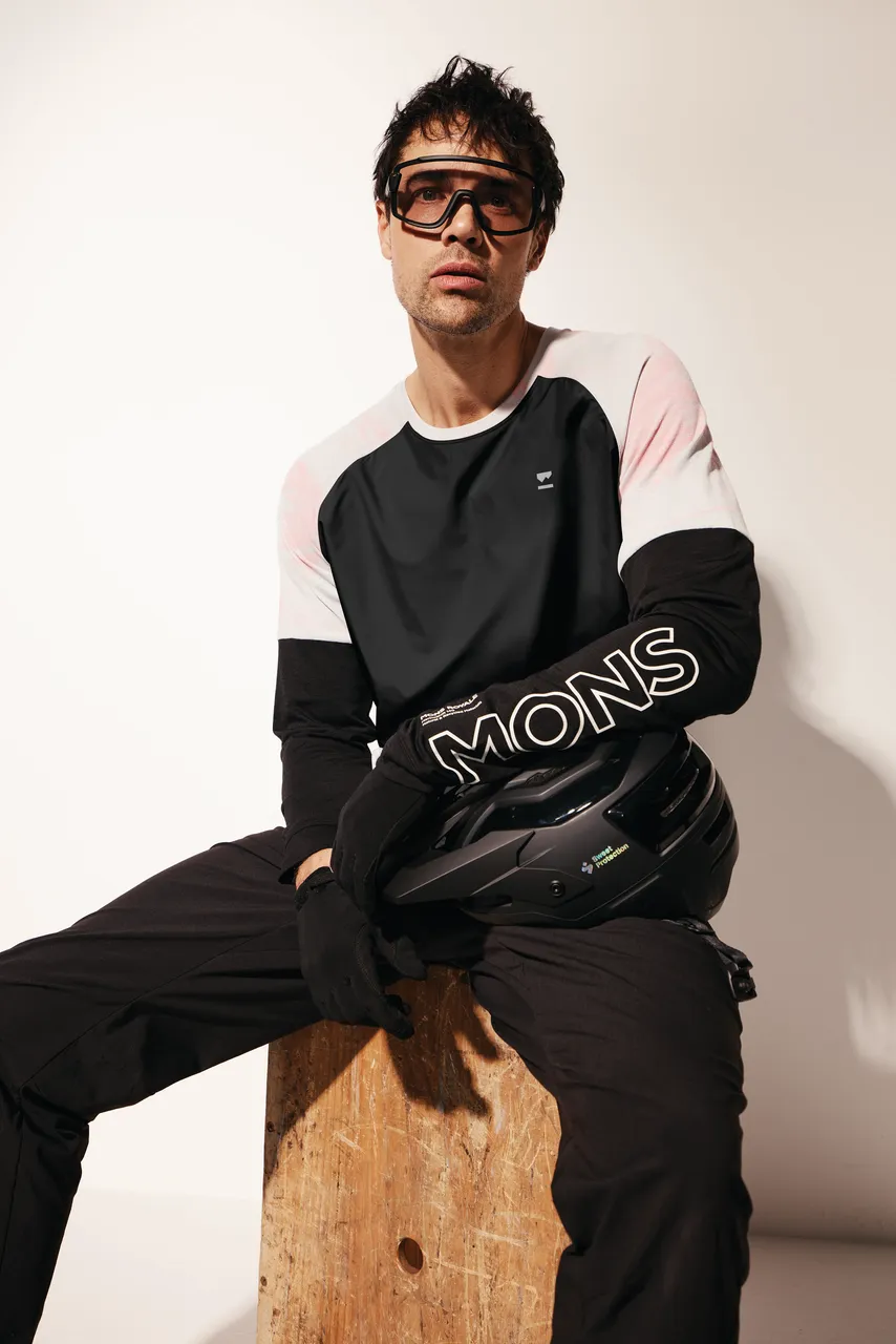 A model in a black and white Mons Royale top sits on a wooden block holding a black helmet.