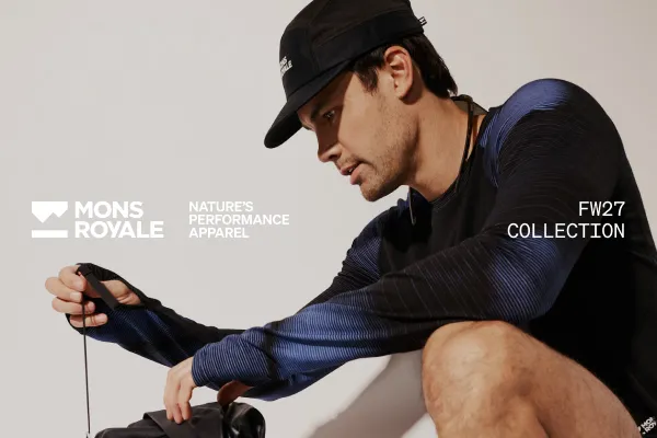 A man in a black cap and navy long-sleeve top adjusts a strap on his outdoor gear.