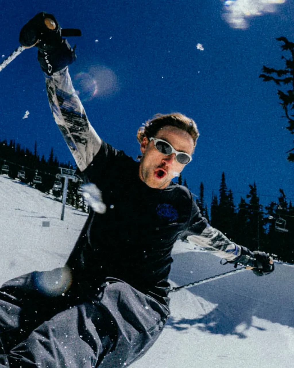 A skier in sunglasses slides down a snowy slope with one ski pole raised.