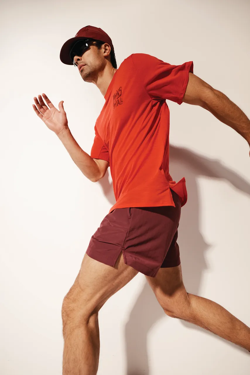 Man runs in a red T-shirt and burgundy shorts, wearing a red cap and sunglasses.