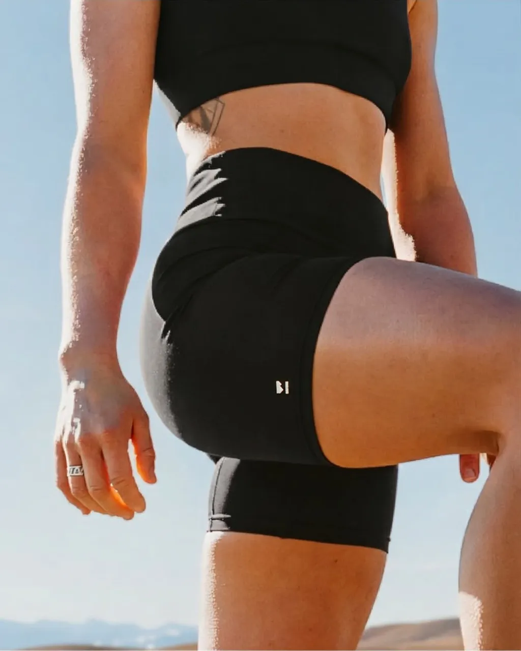 Athlete in black cycling shorts and a crop top poses outdoors in the sun.