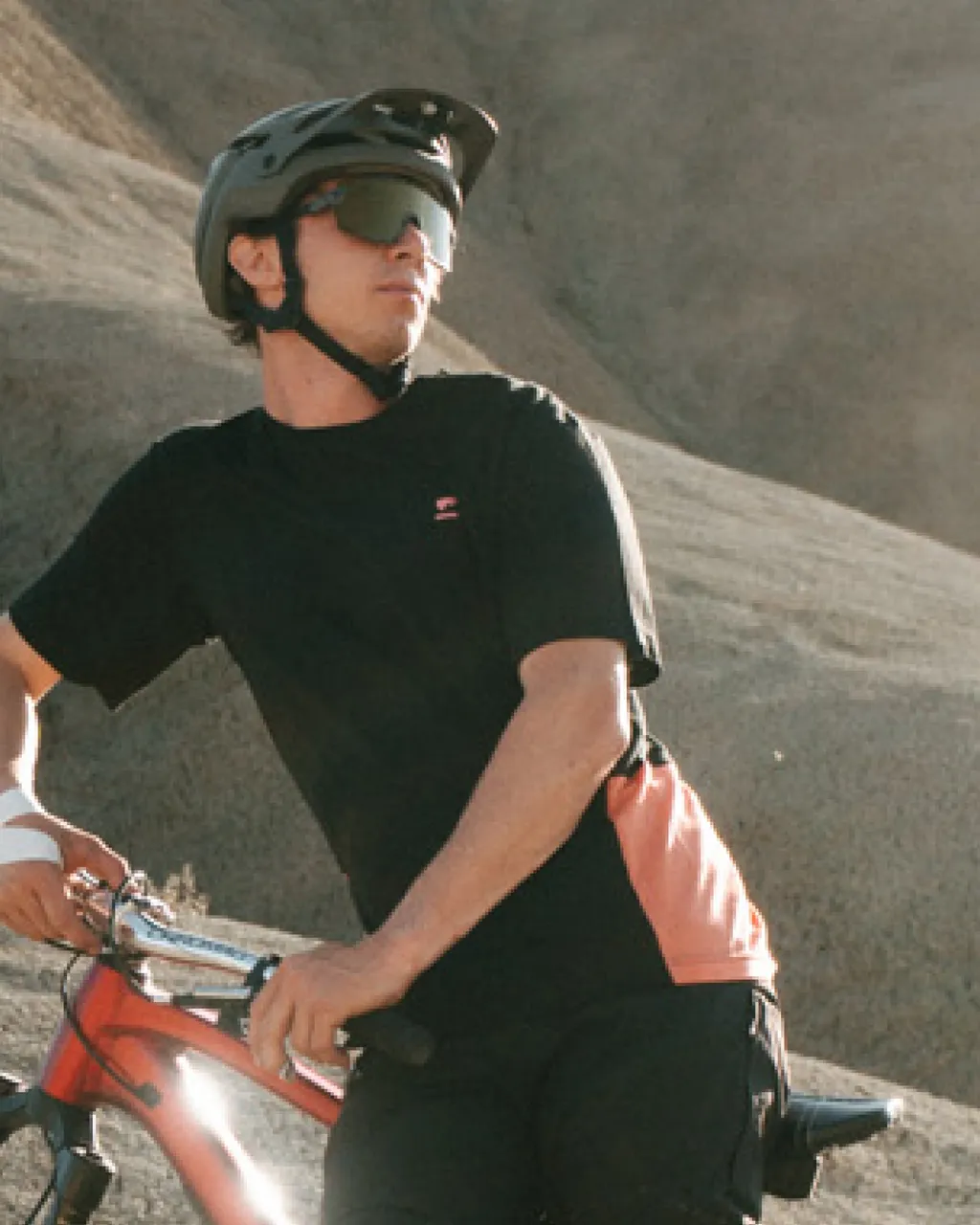 A mountain biker in a black jersey, helmet and sunglasses rides a red bike on a rocky trail.