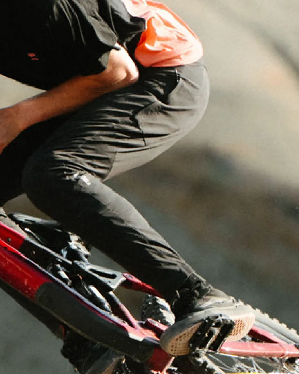 A mountain biker in black pants and an orange top rides a red bike on a trail.