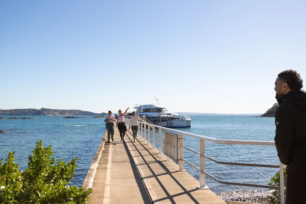 Women walk down wharf with Ferry in background