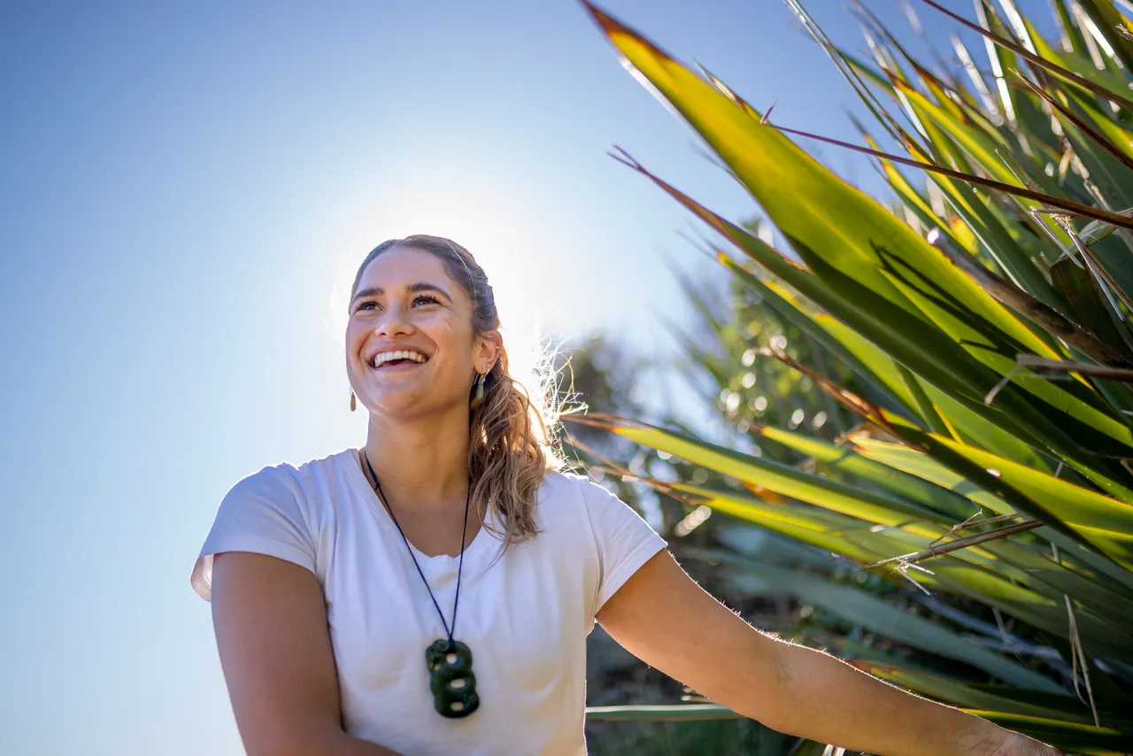 Woman smiles while admiring flax bush