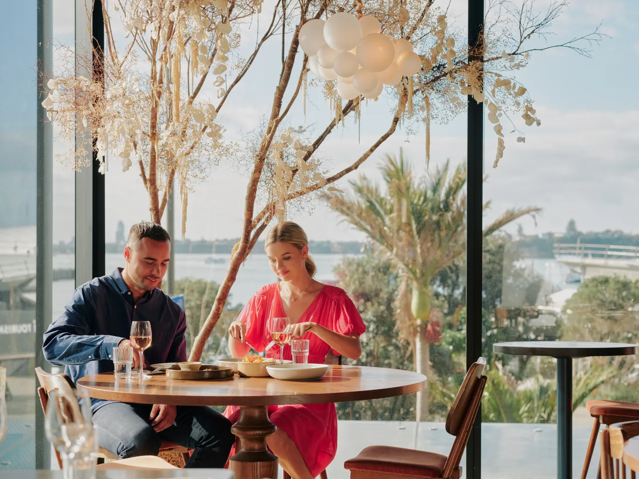 Couple dining at restaurant with Waitematā Harbour in the background