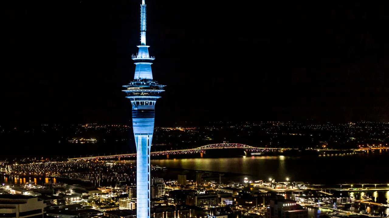 Sky Tower lit up blue with Auckland Harbour Bridge light show in background
