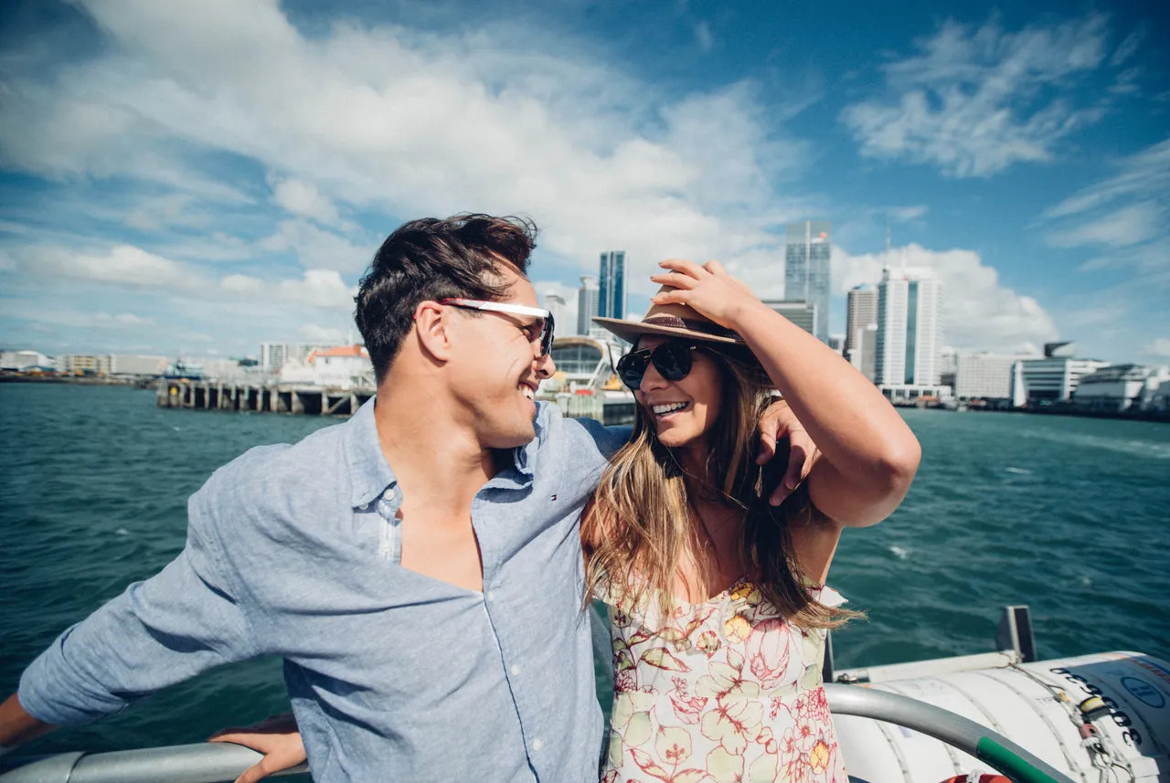 Couple smiling on a boat with Auckland City in the background
