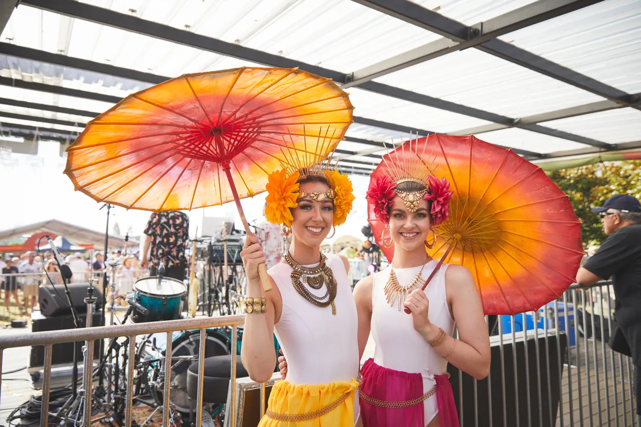 Two girls dressed up with colourful parasols behind stage