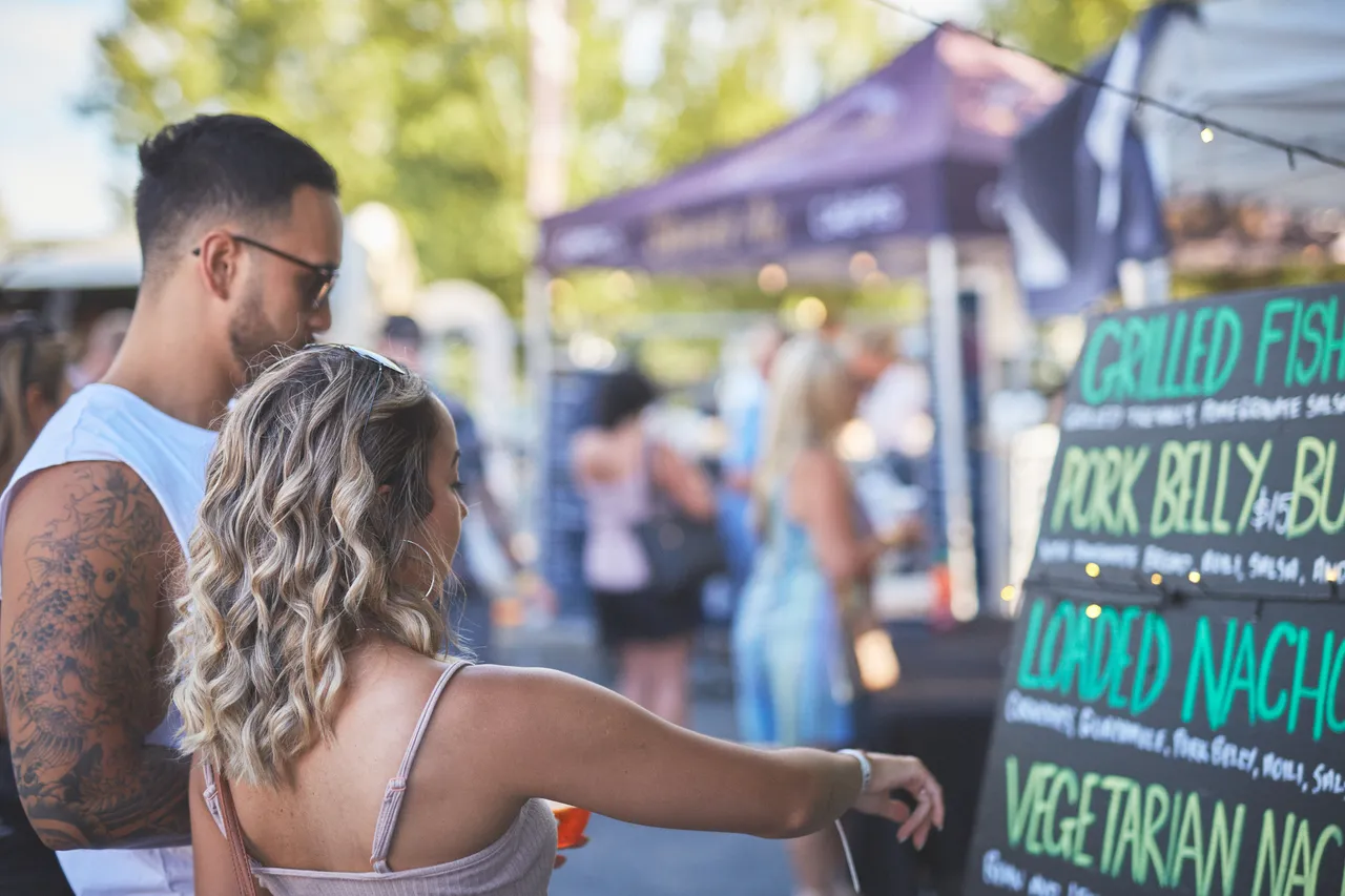 Man and woman looking and pointing at menu at food stall