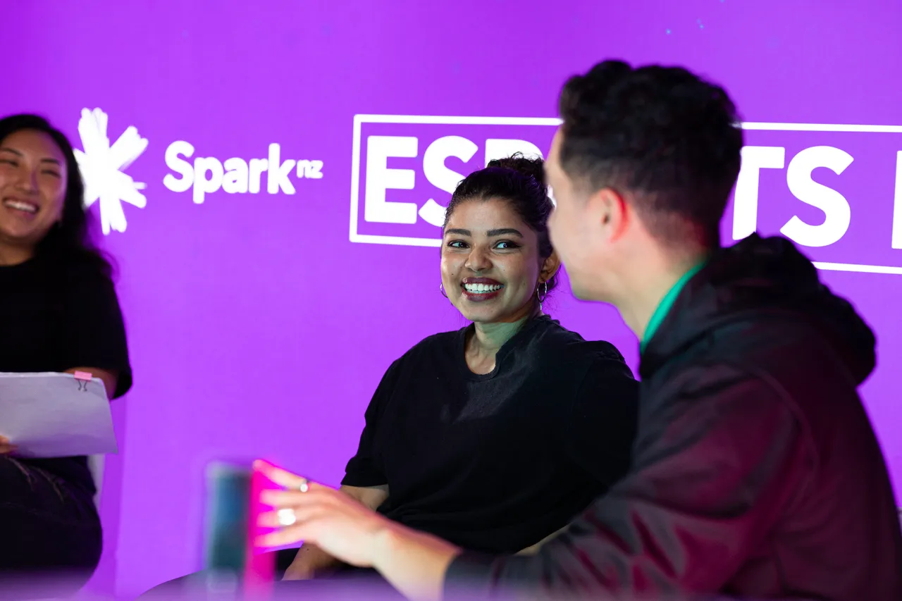Three young people smiling and chatting in front of Spark NZ sign