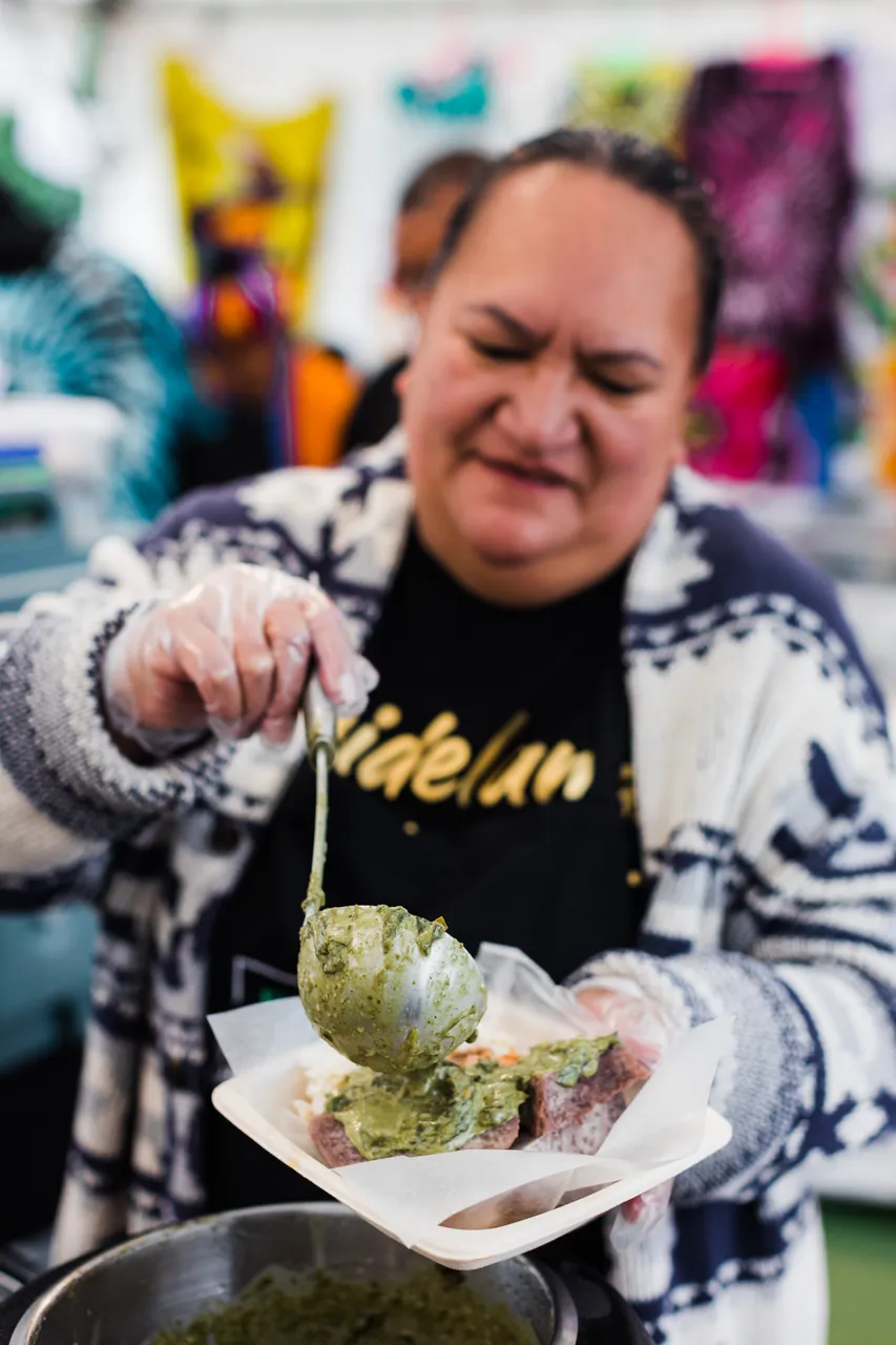Pasifika woman serving up rukau and taro on takeaway plate