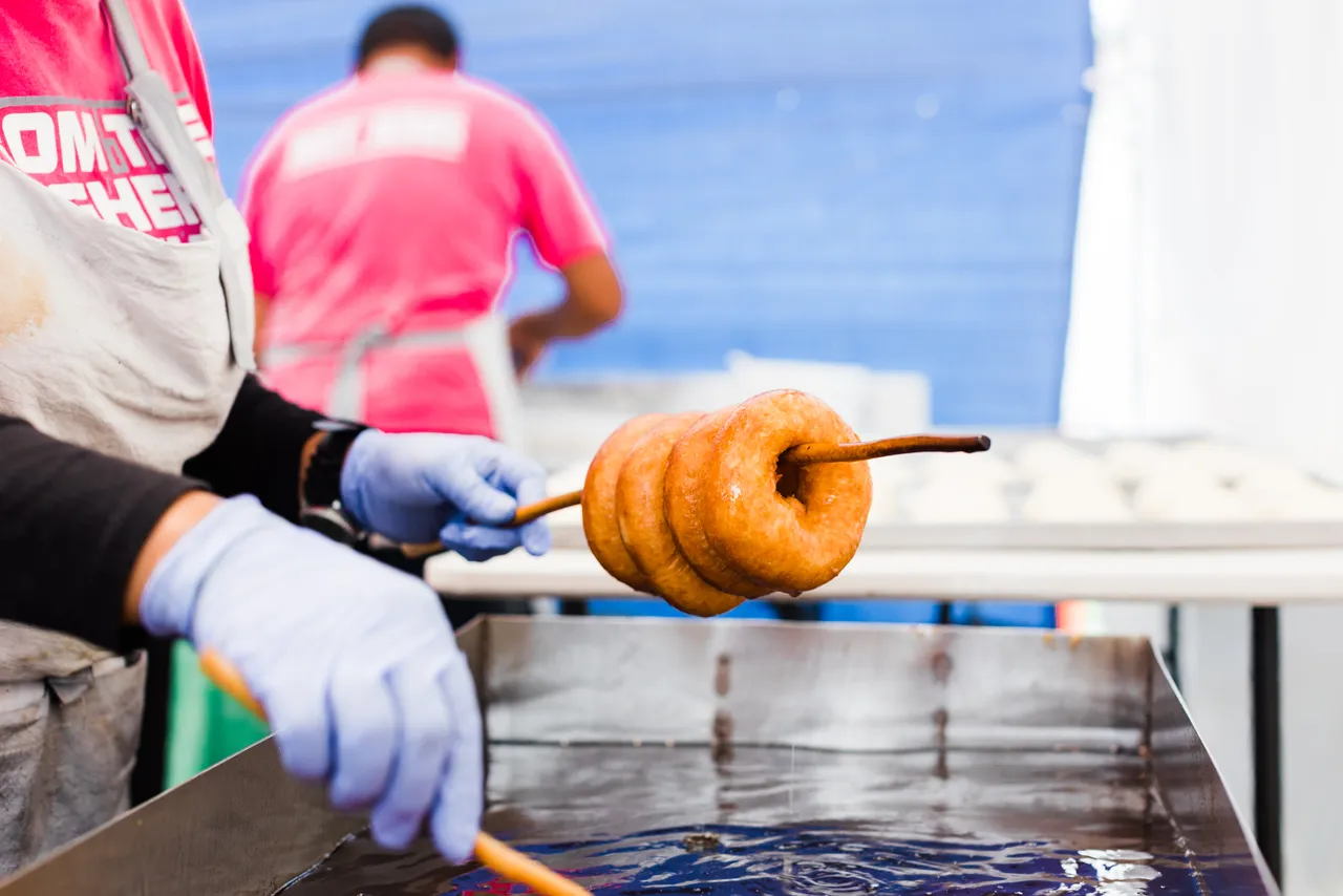 Person holding up stick with freshly fried donuts over deep frier