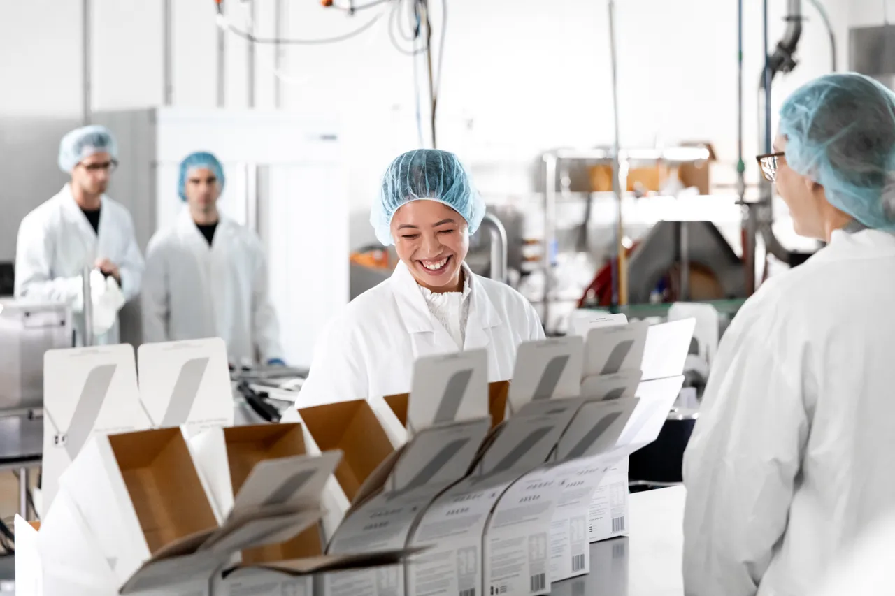 Woman working with boxes in production factory with background workers