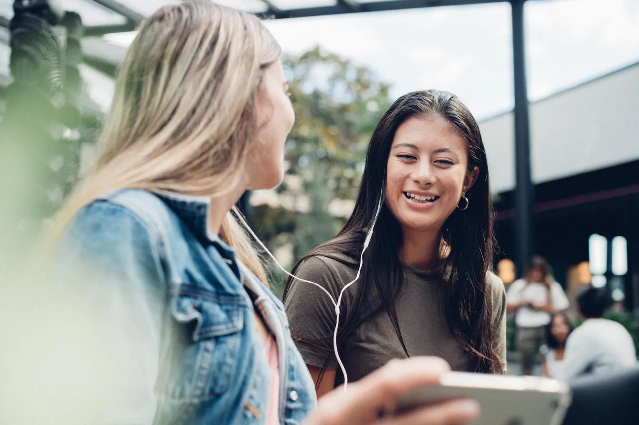 Two girls interacting with each other while using phone