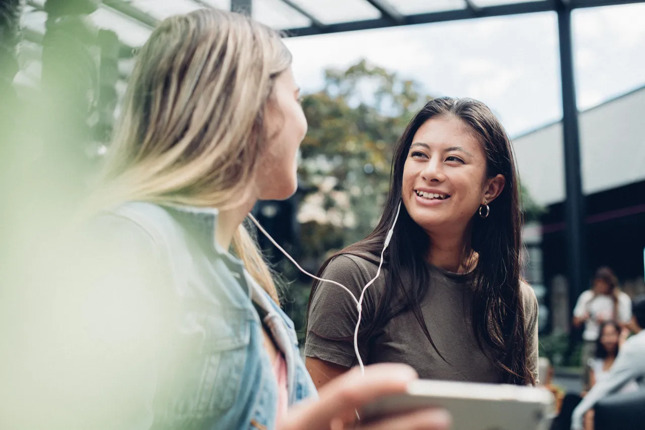 Two girls interacting with each other while holding phone