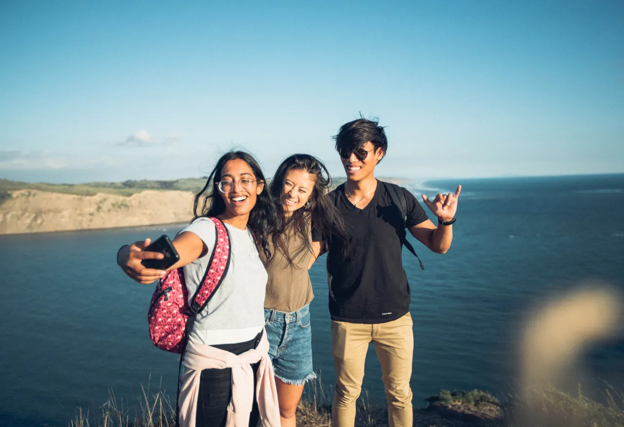 Two girls and a boy taking selfies on a cliff top