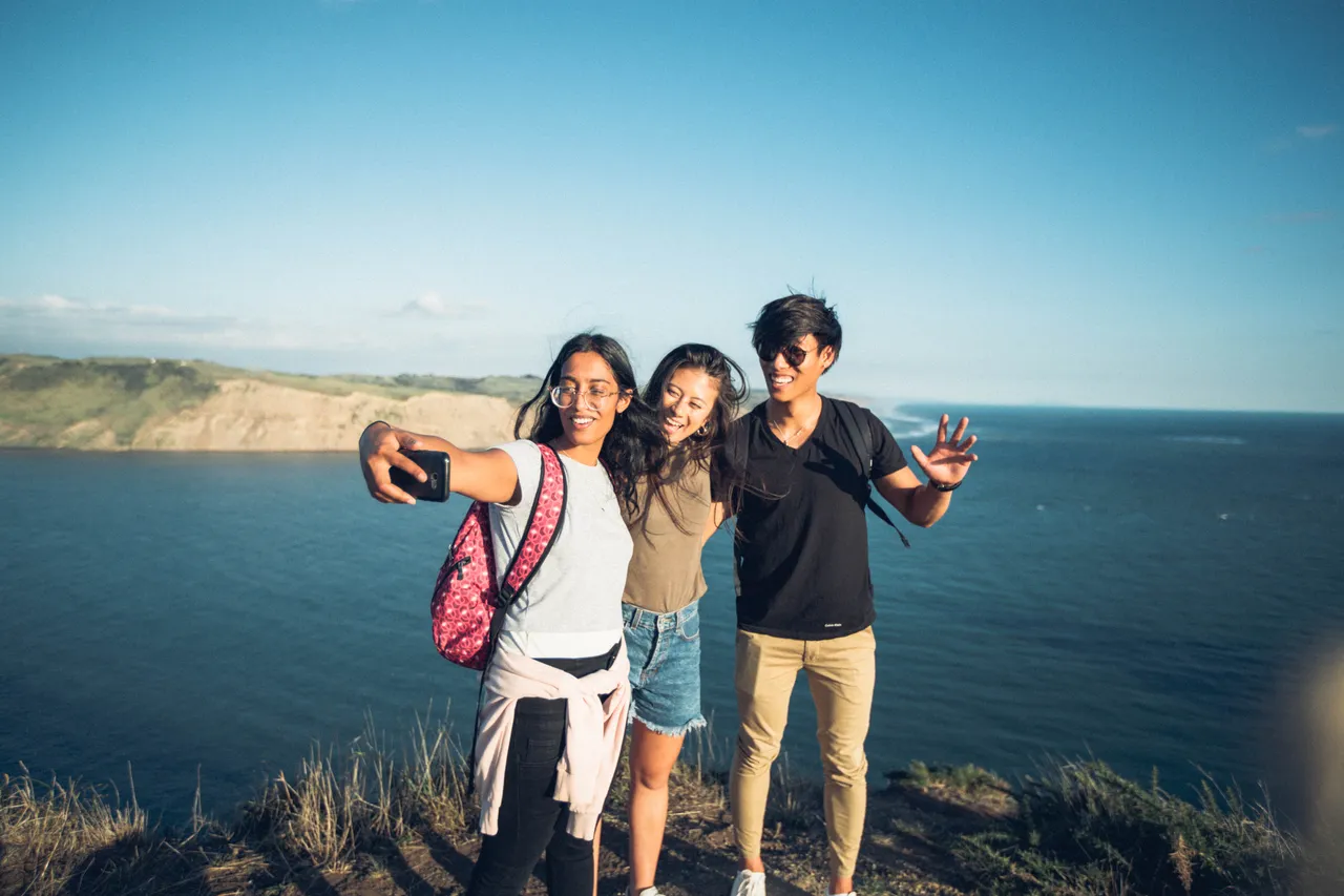 People taking selfies on a cliff next to the ocean