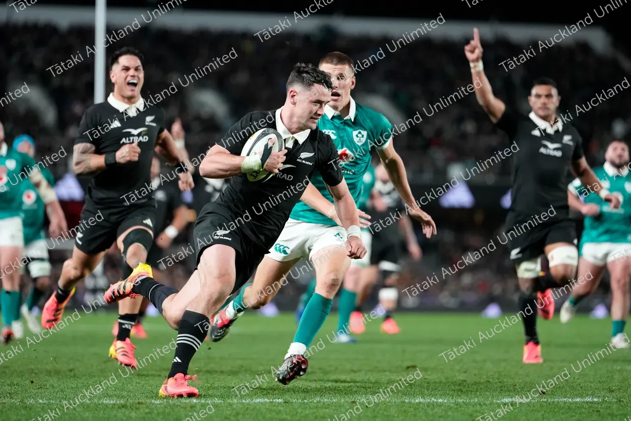A rugby player in black runs with the ball as green-and-white opponents chase him.