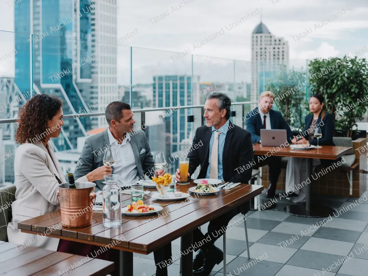 Business professionals dine on a rooftop terrace with city skyline views. 