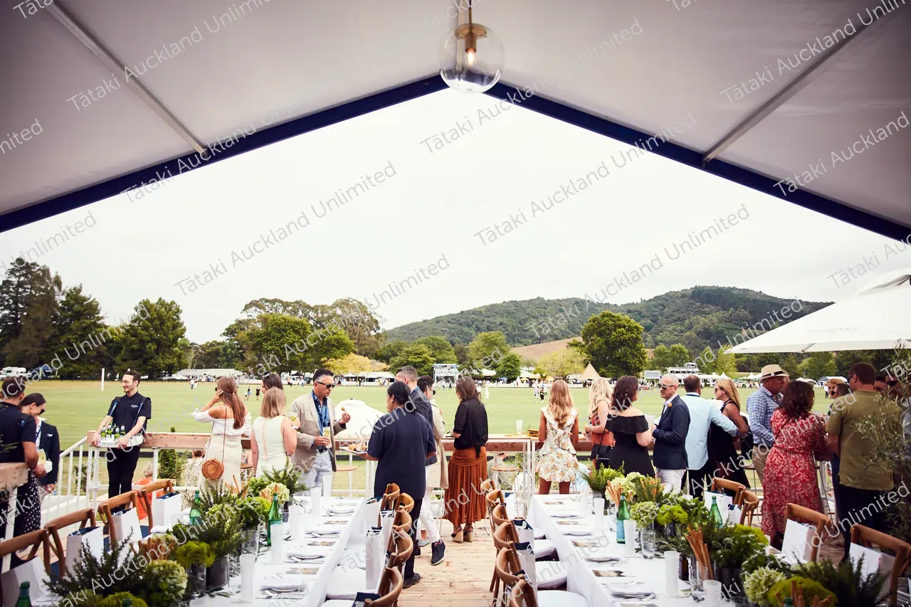 Guests mingle beside decorated dining tables at an outdoor event in a park.