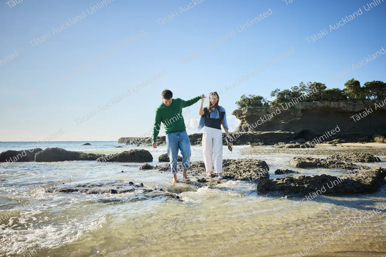 Couple walk on Tāwharanui Beach 