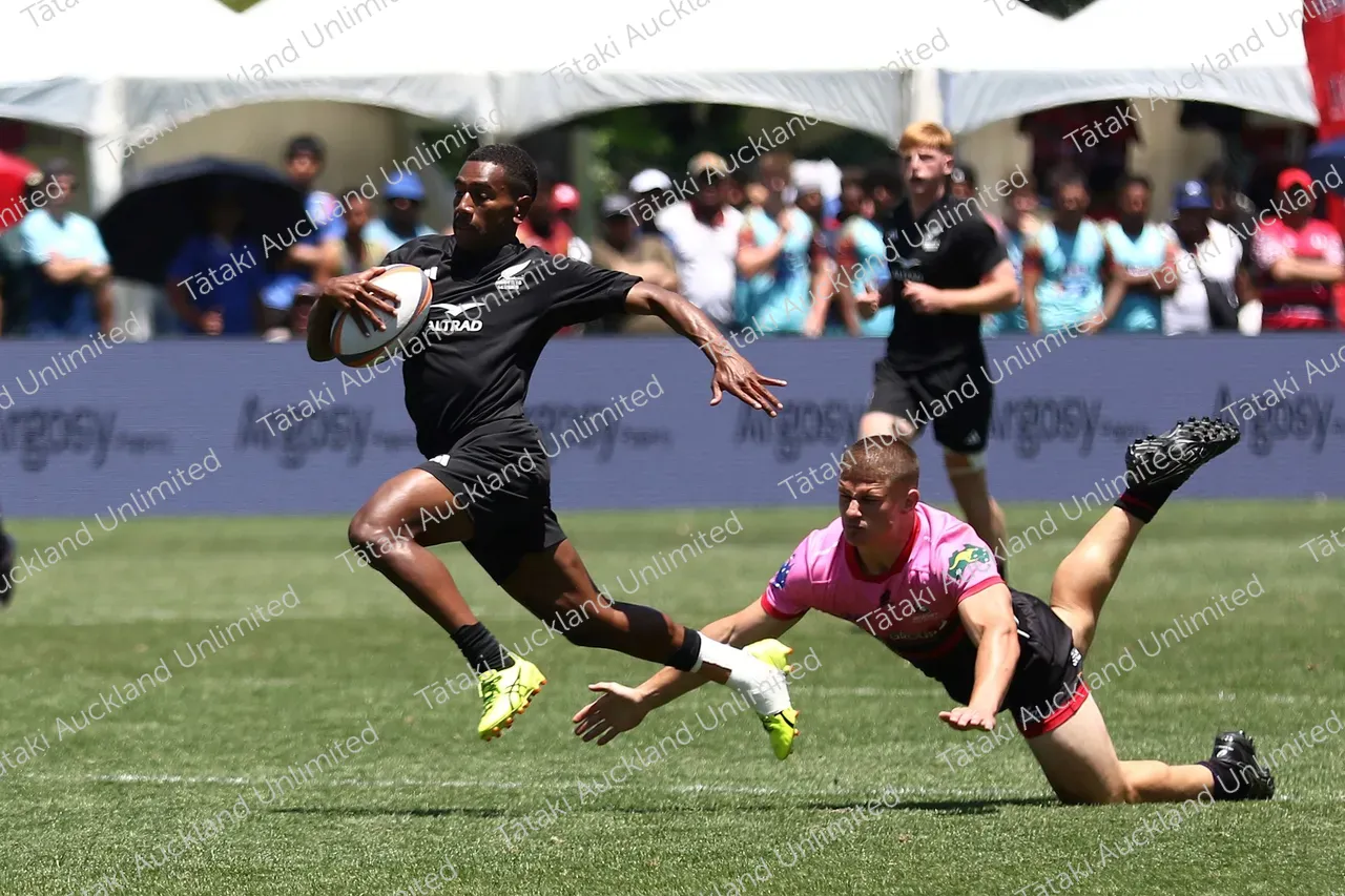 A black-clad rugby player runs with the ball as a pink-shirted opponent dives for a tackle.