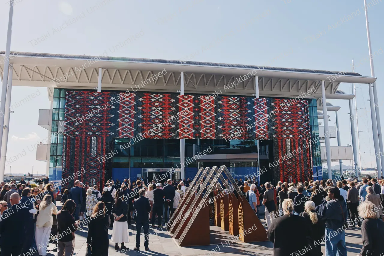 A crowd gathers outside a modern venue beneath a large red, black and white patterned display.