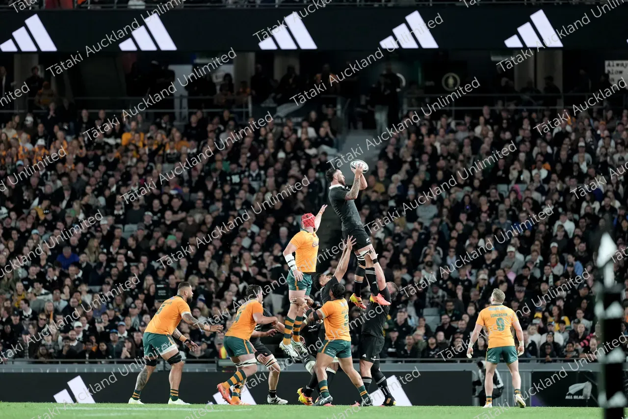 A black-clad rugby player jumps to catch the ball over Australia players during a lineout.