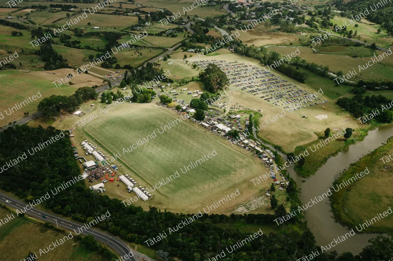 Aerial view of a large event field with tents and parked cars beside a winding river.