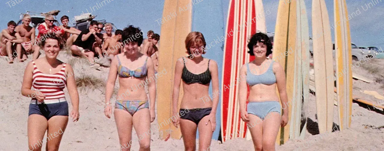 1960s image of women in swimwear with surfboards and men in background