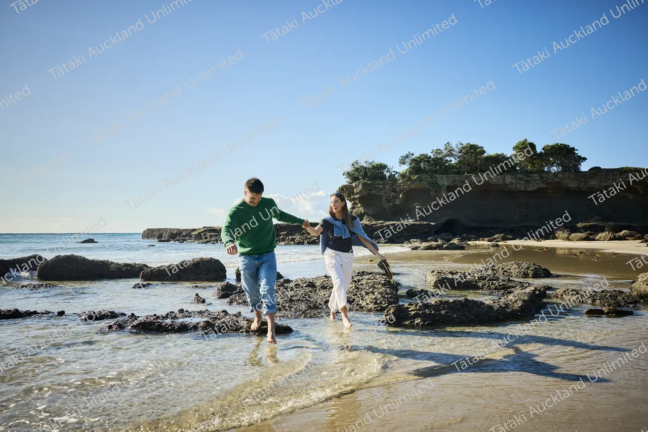 Couple walk on Tāwharanui Beach 2