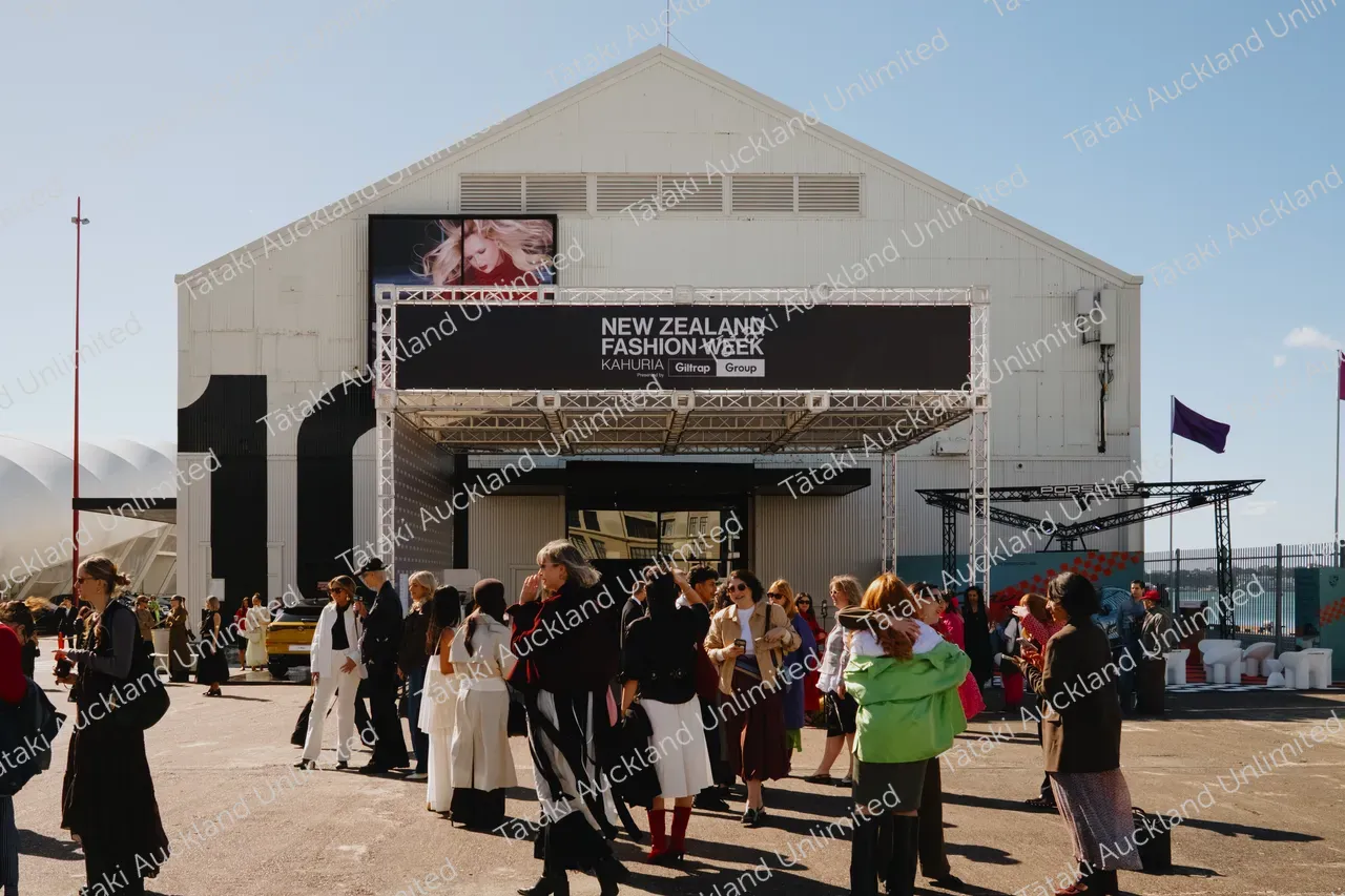 People gather outside the New Zealand Fashion Week venue on a sunny day.
