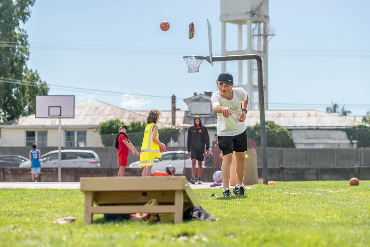 Teenager plays Cornhole by a basketball court