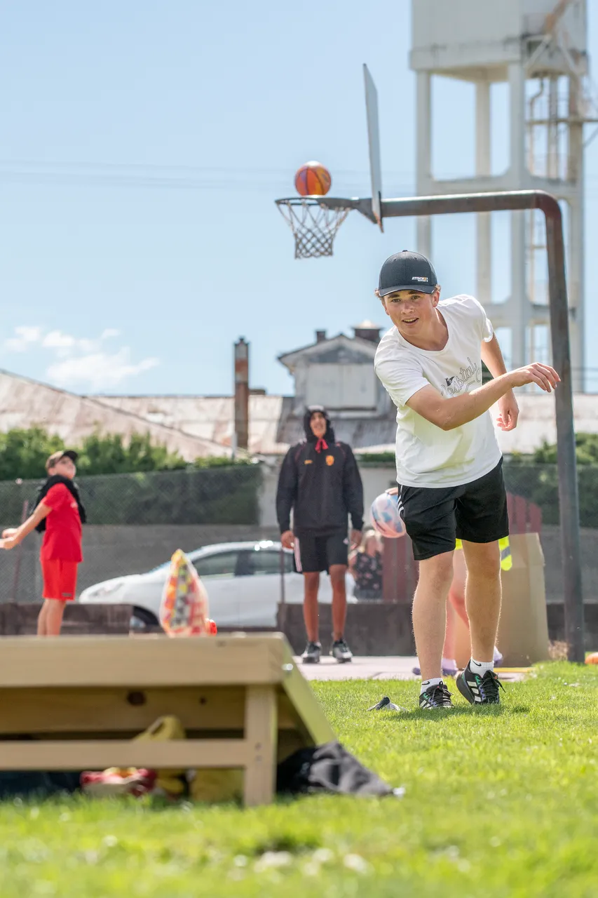Teen plays cornhole beside a basketball court