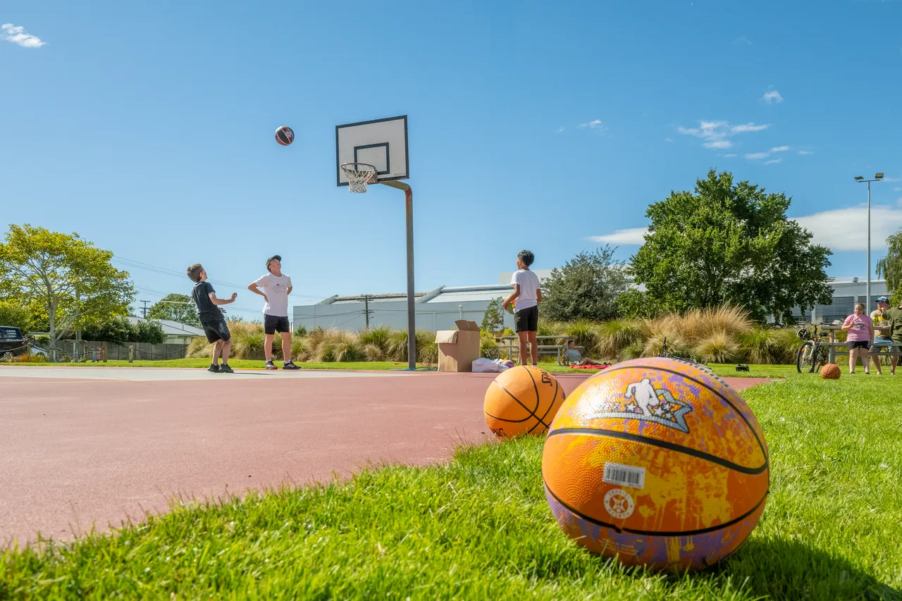 Teens play basketball in background with basketballs sitting in the foreground
