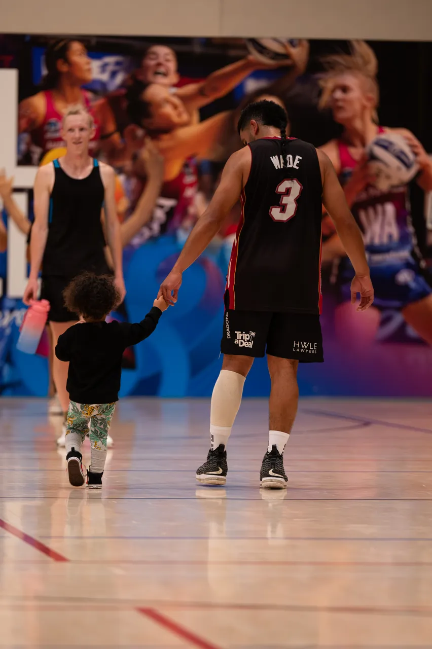 A netball player holding his childs hand on a court