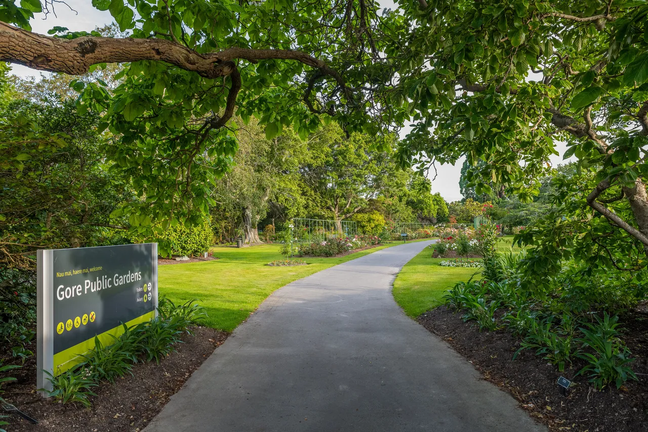 Pathway leading through Gore Public Gardens with lush greenery and a signboard on the left.