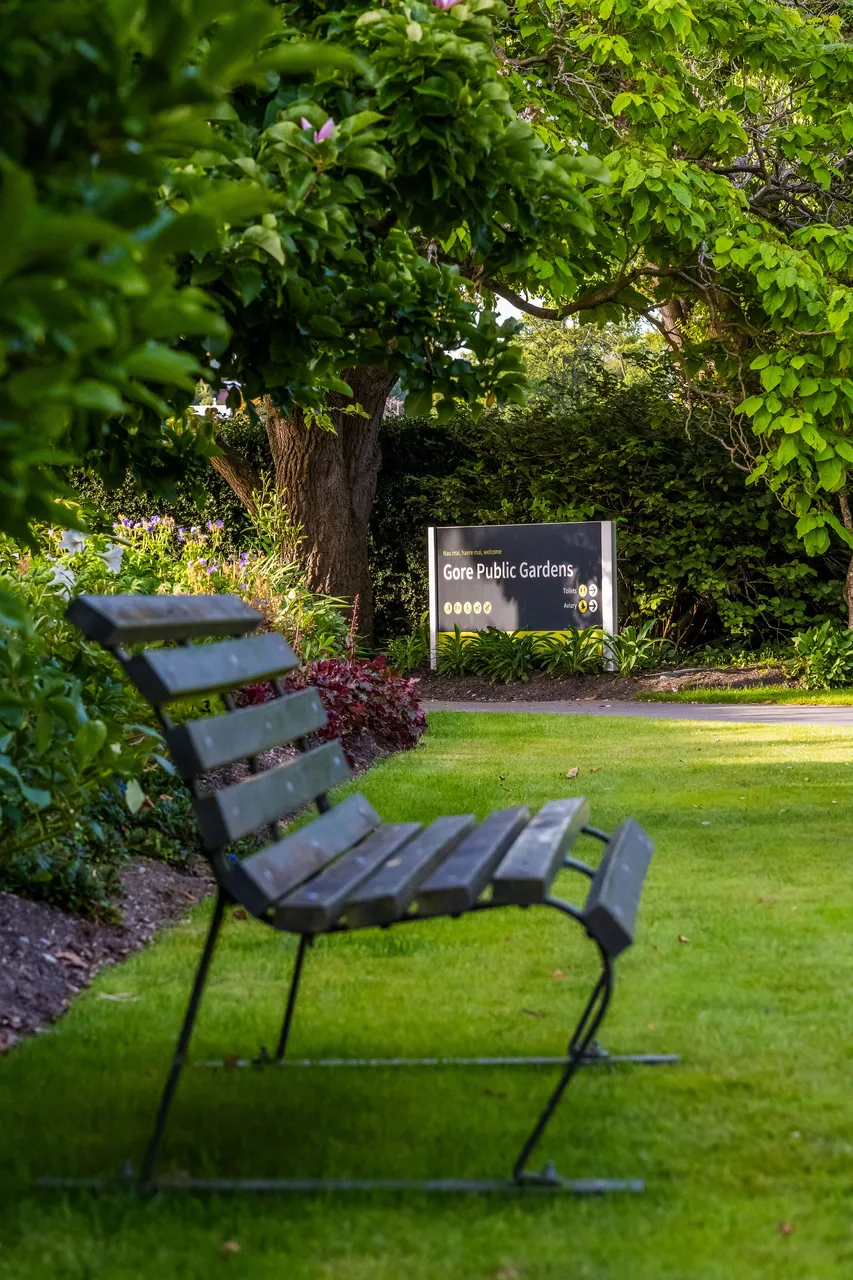 Park bench with "Gore Public Gardens" sign surrounded by greenery.