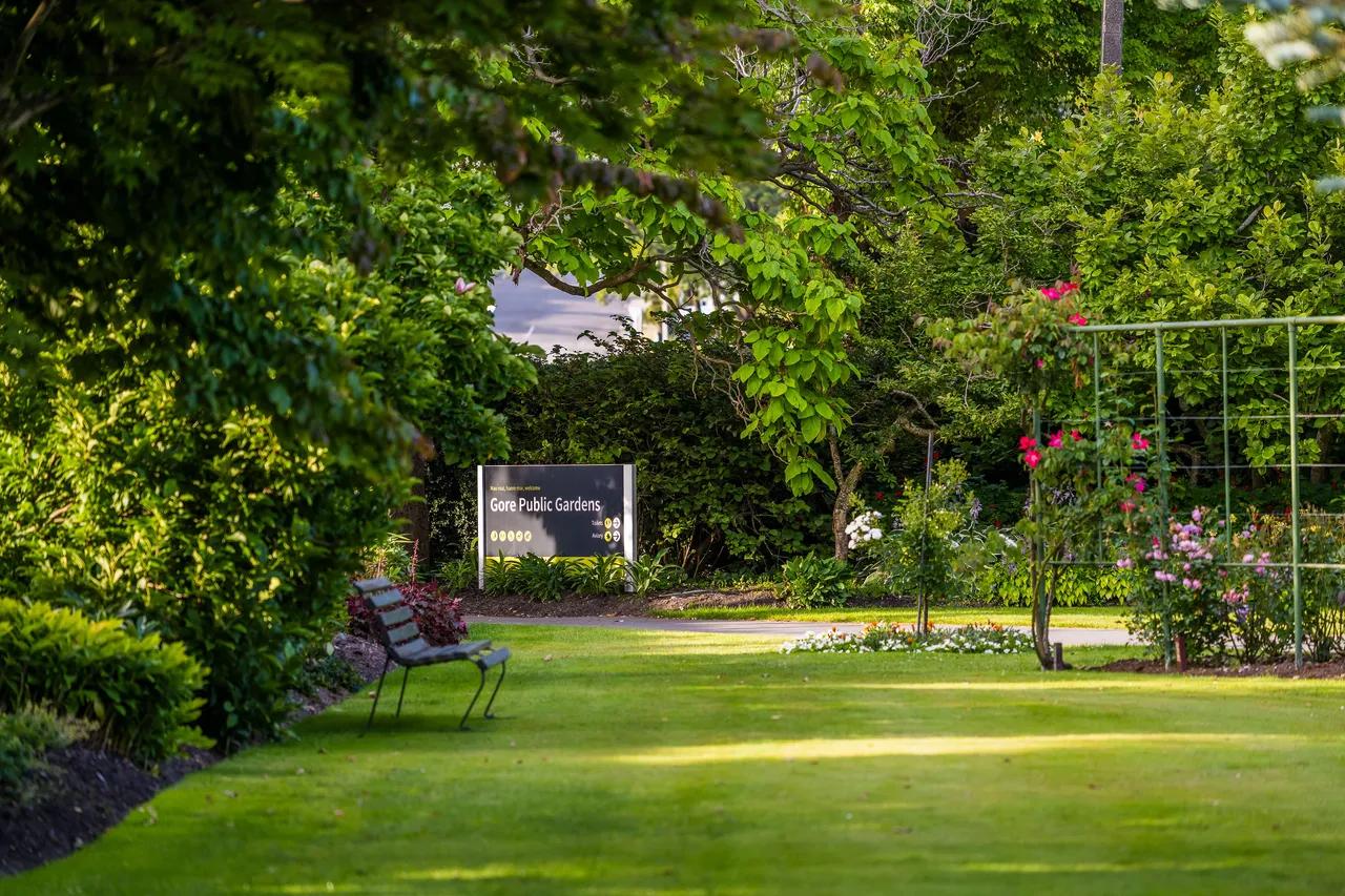 Park bench with "Gore Public Gardens" sign surrounded by greenery.