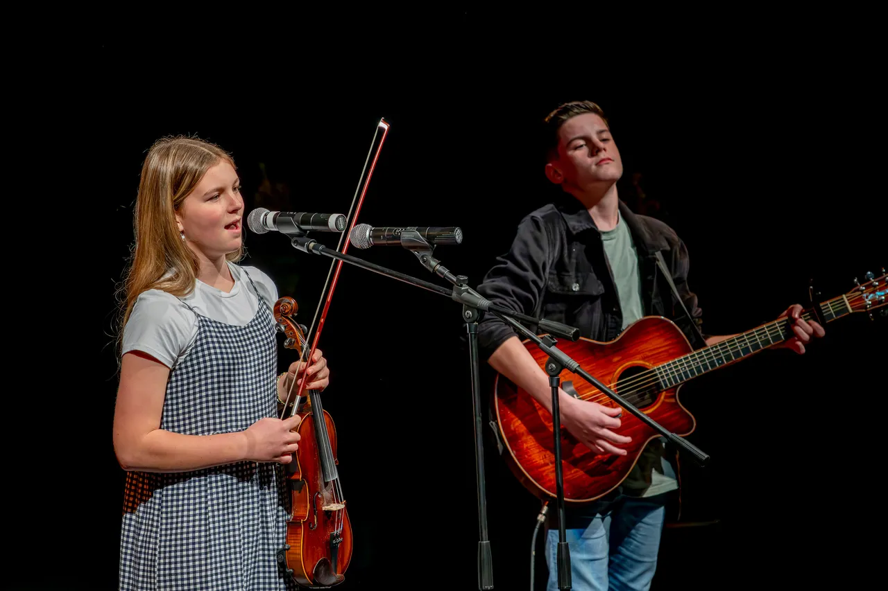 Child plays violin and boy plays guitar on stage
