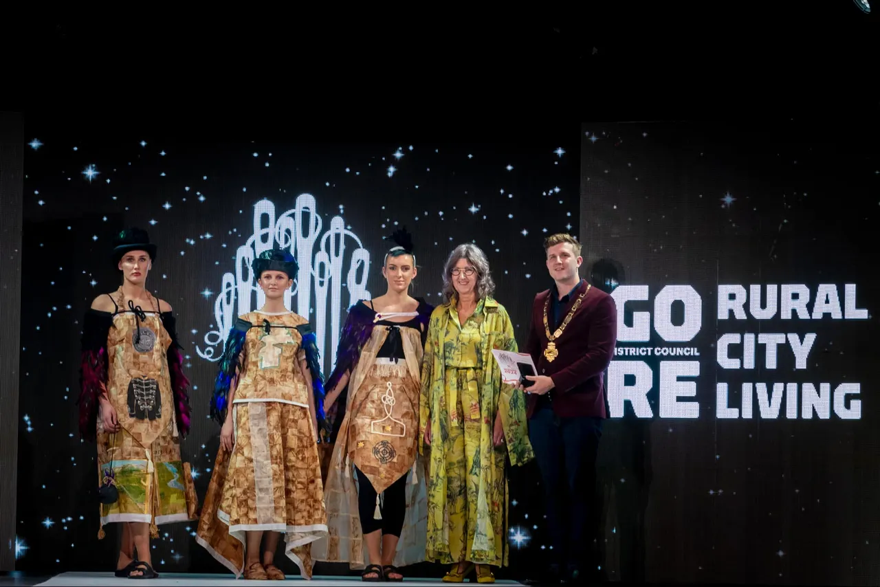Designer on stage with models wearing her award winning dresses