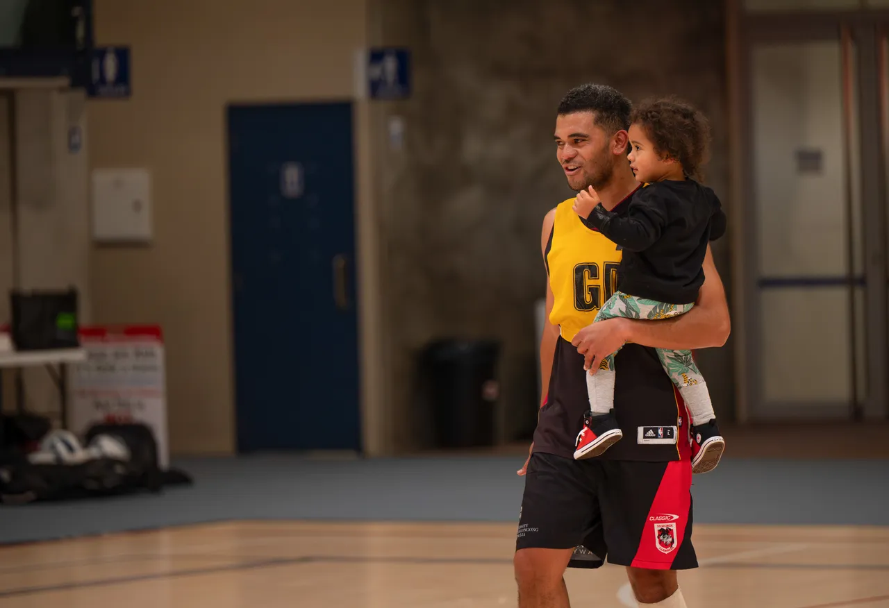 A man holding a child on a netball court