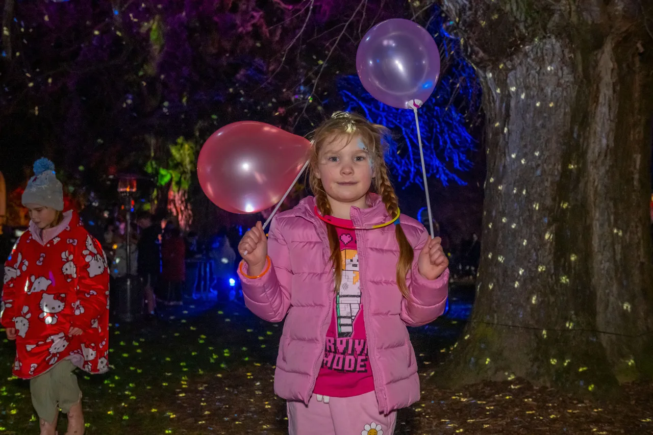Girl holding two balloons and wearing glowsticks.