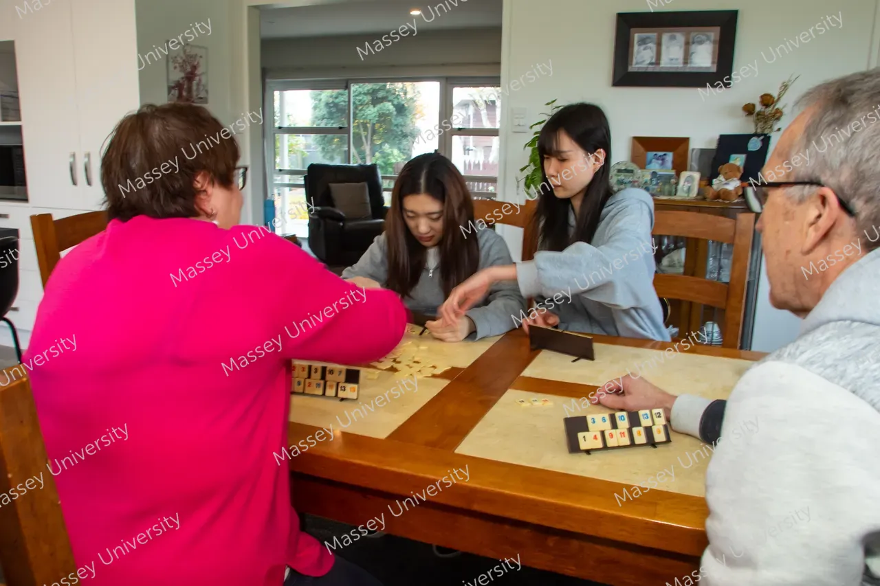 Four people play a tile-based game around a dining table.