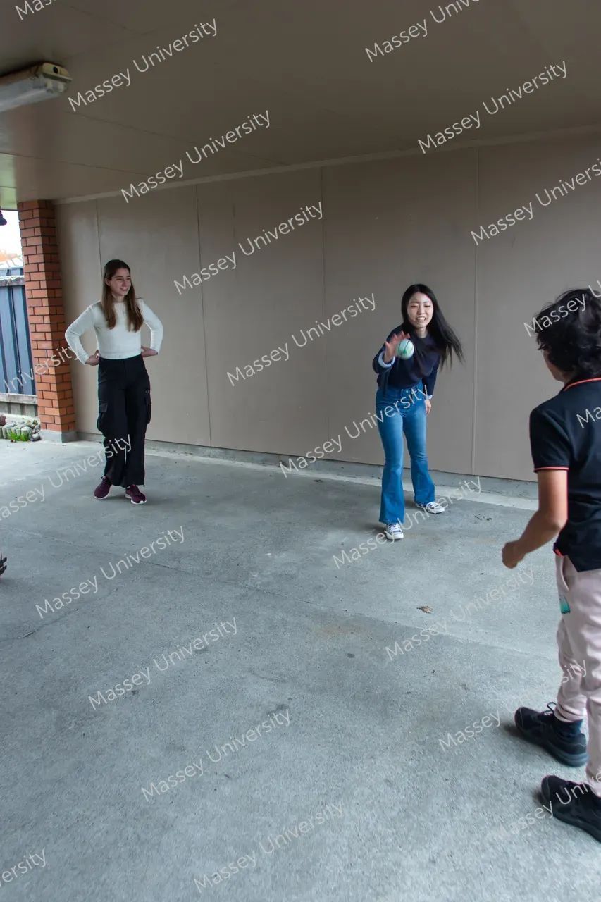 Three students play a ball game in a covered outdoor area.