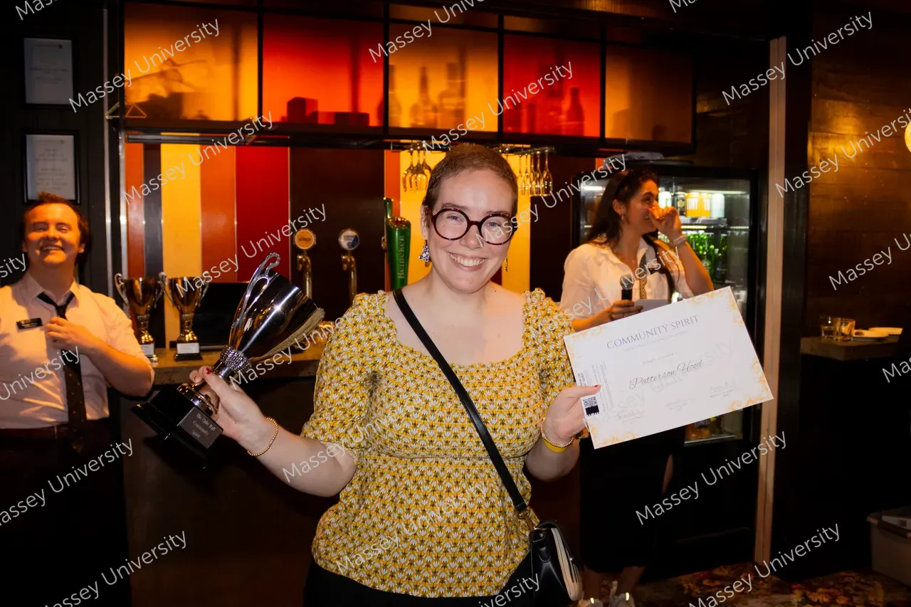 A smiling woman holds a trophy and a large cheque at an awards event.