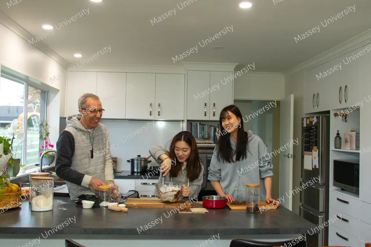 Three people prepare food together at a kitchen island, mixing ingredients in a bowl.